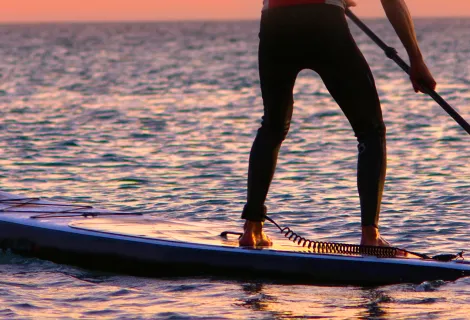 A man paddleboarding at sunset