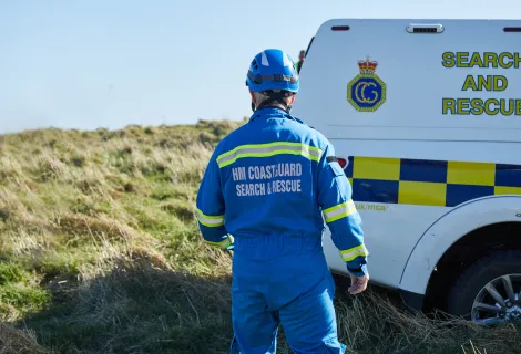 A coastguard rescue officer stands by an HM Coastguard van by a cliff