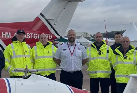 Five men stood between two HM Coastguard aircraft, one man in white shirt between four in high-vis jackets