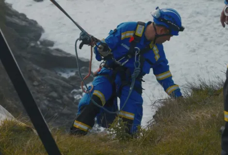 A Coastguard Rescue Officer rope technician carefully goes down over a cliff edge, attached to a rope