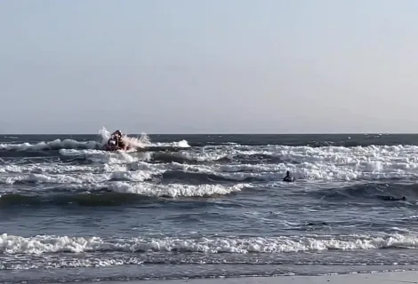 Swimmer in sea with breaking waves and a small lifeboat in distance