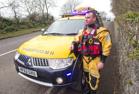 Senior Coastal Operations Officer Ryan Gray in safety kit standing next to an HM Coastguard vehicle