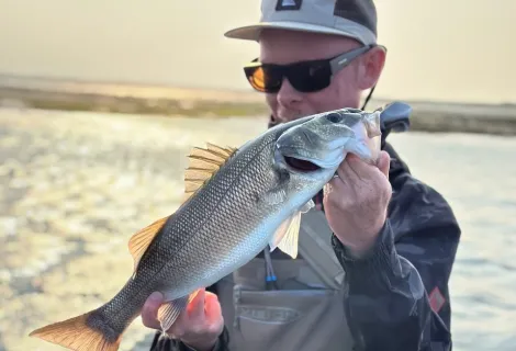Ben Lovell by the coast in his angling gear holding a fish
