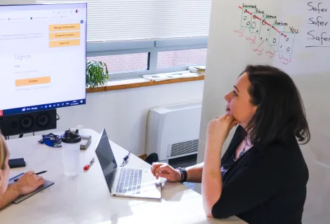 Two office workers on either side of a desk contemplate a screen