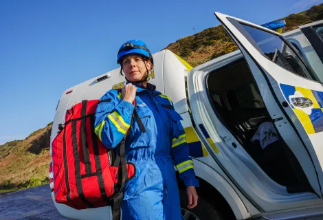 A female coastguard carrying a red bag stands near a vehicle