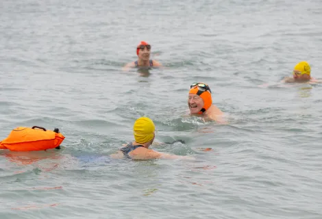 Swimmers in the sea wearing bright headcaps and one towing a float