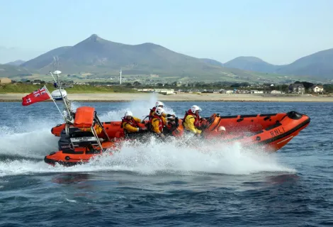 orange lifeboat speeding through the water with mountains in the distance