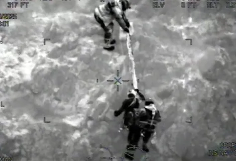 Night-vision image of a climber on a rope being helped up the cliff by two Coastguard Rescue Officers
