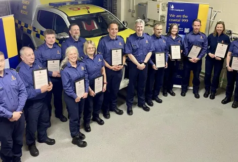Smiling Coastguards in blue uniforms hold their awards with Assistant Chief Coastguard John Craig standing in the middle