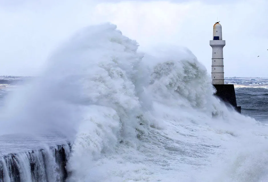 Waves crashing on the coast in front of a lighthouse