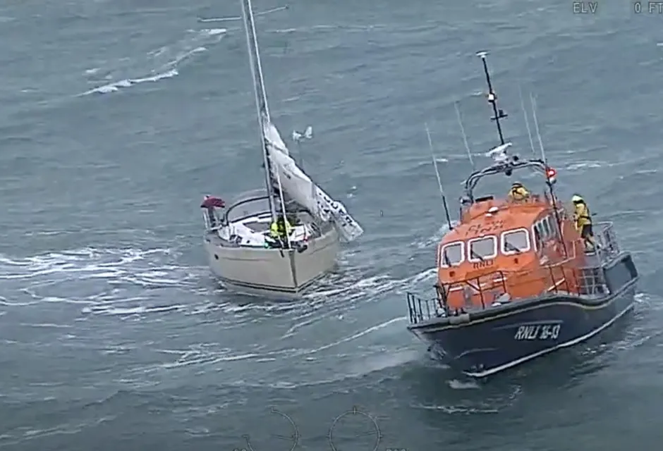 White sailing yacht and orange and blue RNLI vessel in stormy waters