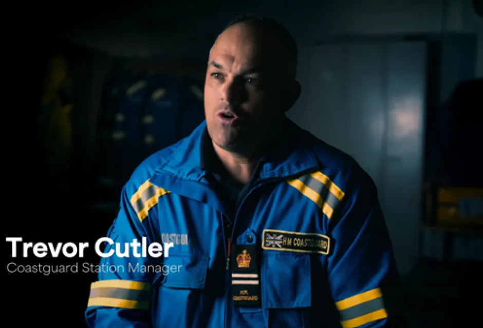 Screenshot from TV series of Coastguard officer in uniform sat in front of a darkened background