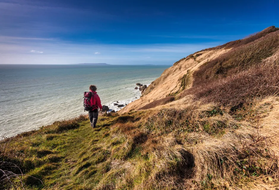 Man in hiking clothes and backpack walking along coastal path with sea in background