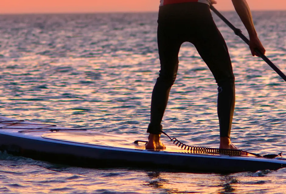 A man paddleboarding at sunset