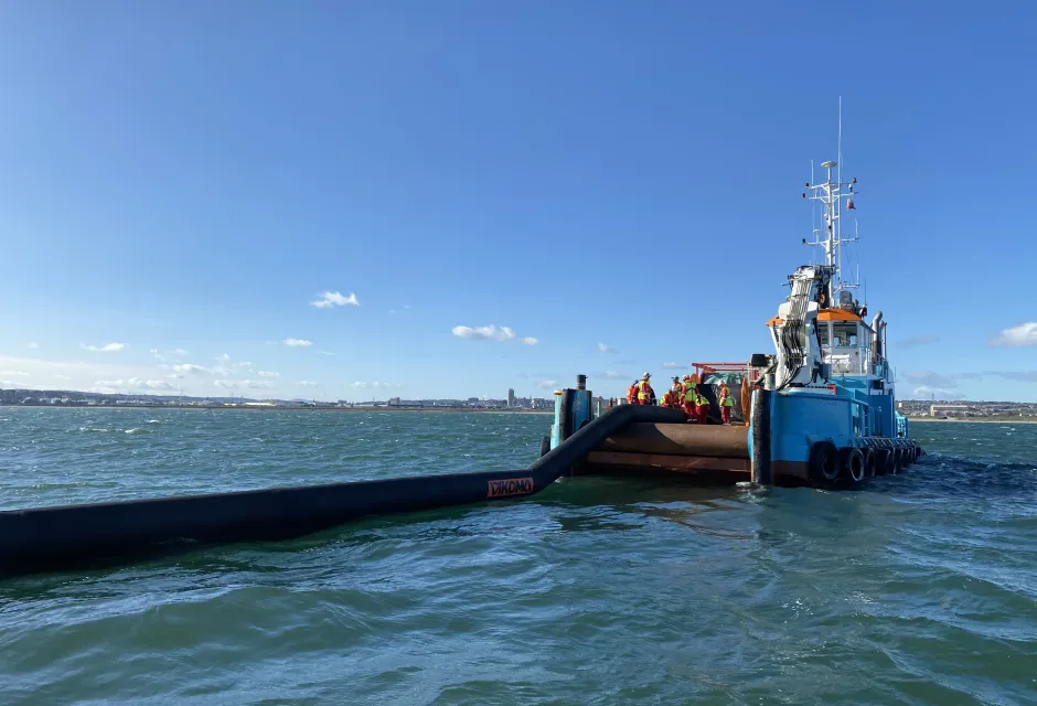 A counter-pollution boom is delivered from the back of a vessel in the sea off Aberdeen