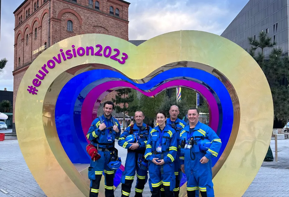 Five coastguards in uniform posing in front of Eurovision stand in Liverpool