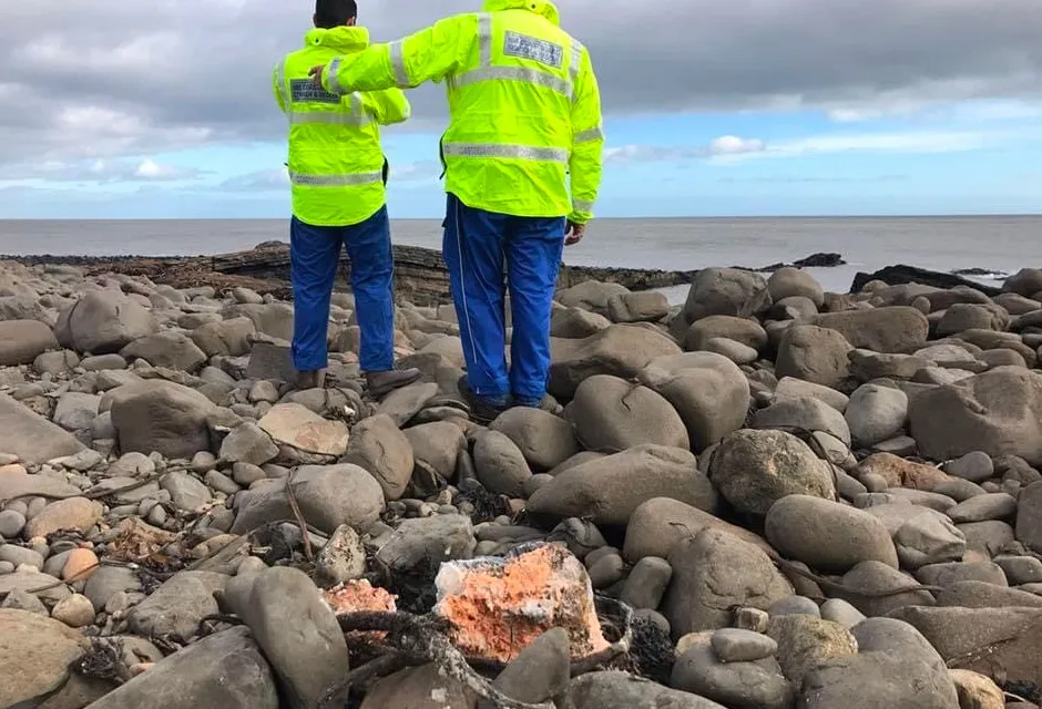 Man in high vis carefully examining a white substance on rocky pebbles