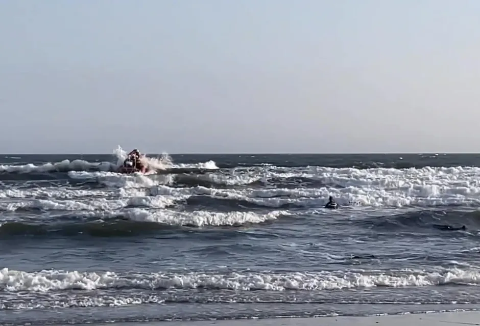 Swimmer in sea with breaking waves and a small lifeboat in distance
