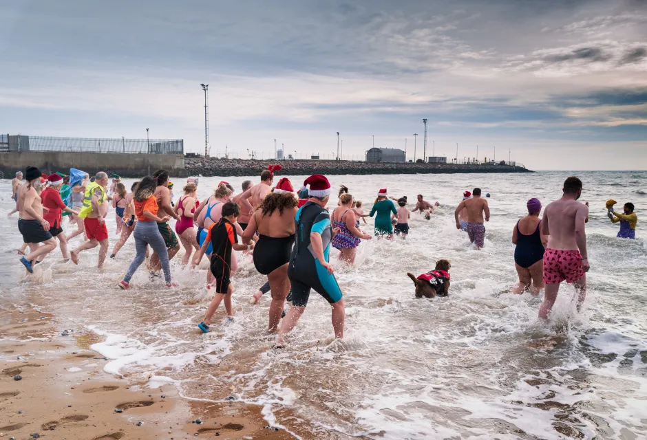 Swimmers running into a wintery sea at Ramsgate, some wearing Christmas hats