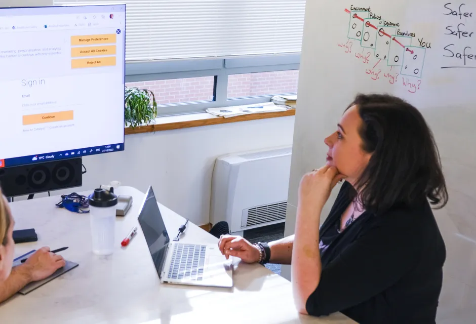 Two office workers on either side of a desk contemplate a screen
