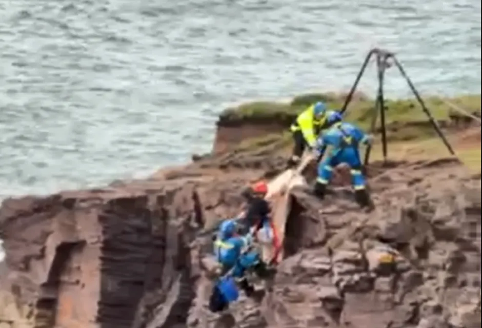 Coastguard rope technicians help a boy to the top of a sea cliff