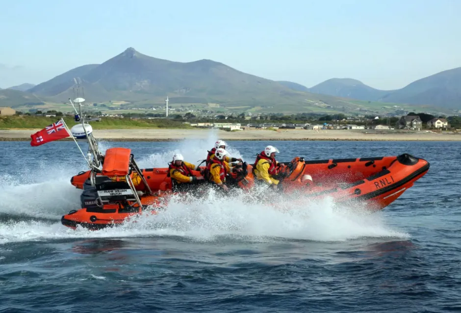 orange lifeboat speeding through the water with mountains in the distance