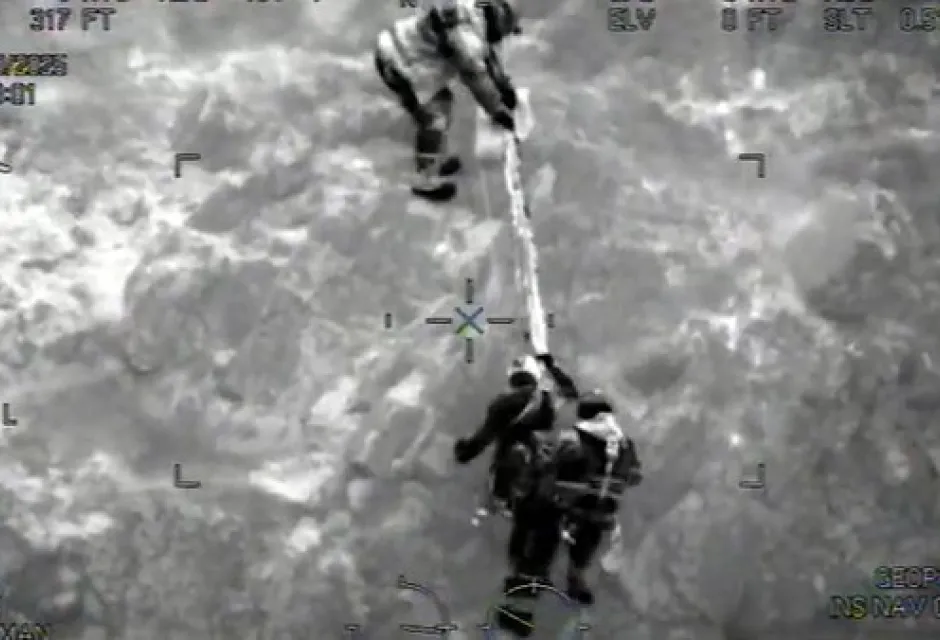 Night-vision image of a climber on a rope being helped up the cliff by two Coastguard Rescue Officers
